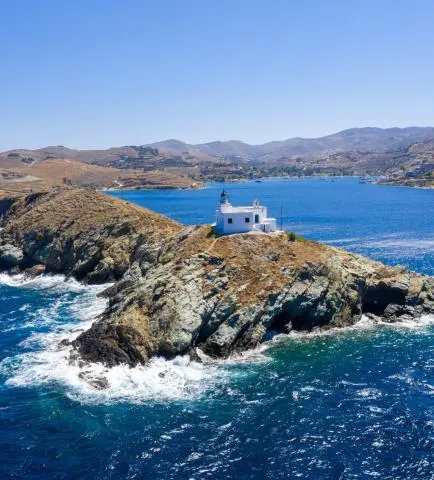 White lighthouse on a rocky promontory with waves crashing into deep blue sea