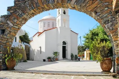 White church with bell tower framed by a stone arch, potted plants in courtyard