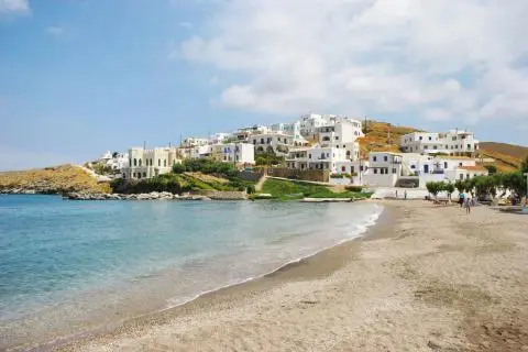 Sandy beach in foreground with clear blue water and white houses clustered on a hillside