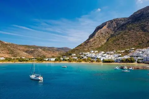 White sloop anchored near a sandy bay with turquoise water and hillside white houses