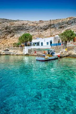 Small boat moored at a stone quay beside a white coastal house over turquoise water
