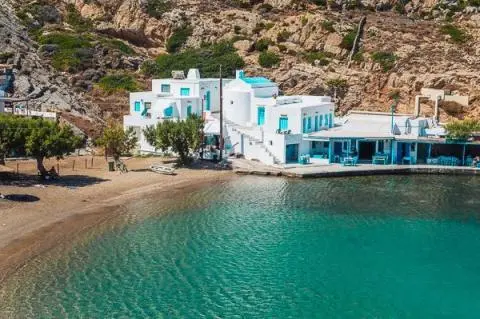 White and blue seaside buildings beside clear turquoise water and a small sandy beach
