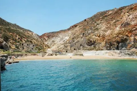 Turquoise sea in foreground, small sandy beach and rocky hills with old stone buildings