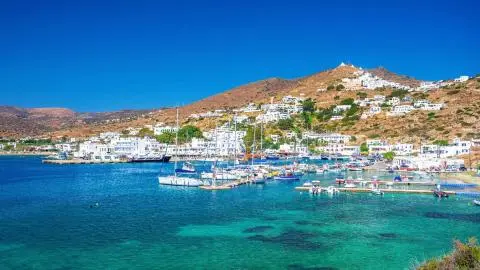 Sunlit yachts docked in a harbor with white buildings on a hillside