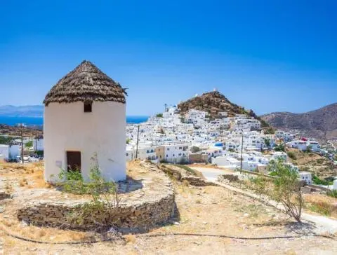 Small stone windmill and hillside village with white buildings under blue sky
