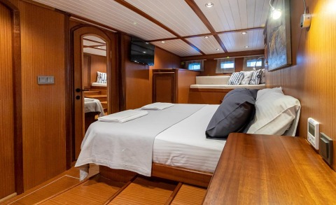 Bodrum Queen luxury yacht interior: wood-paneled cabin with a large bed, navy and white linens, and a seating area in the background.