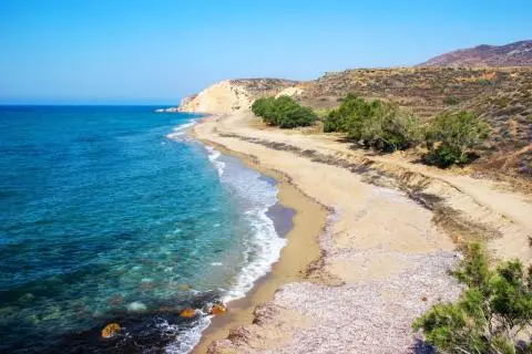 Turquoise sea with waves lapping a sandy shoreline, trees and rocky cliffs in background