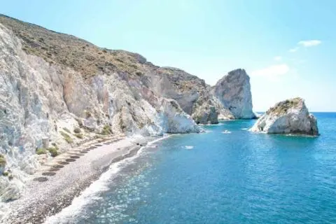 Clear blue sea beside white rocky cliffs and a pebble beach with prominent rock formations