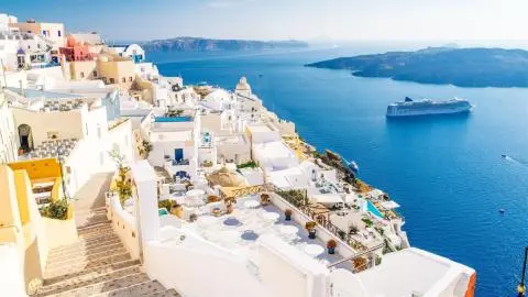 Cliffside white buildings, terraces and stairs overlooking deep blue Aegean Sea with a cruise ship
