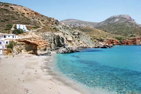 Turquoise bay with sandy beach, rocky cliffs and white-blue houses on a Greek island