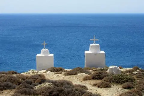 Two small white chapel columns with crosses on a scrubby coastal cliff overlooking deep blue sea