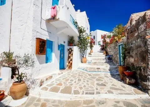 Whitewashed Mediterranean alley with blue door and shutters, stone steps, potted plants and flowers