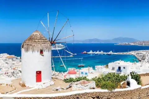 Whitewashed windmill by the blue Aegean Sea with yachts anchored in the harbor