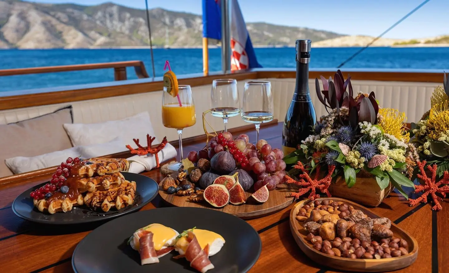 Yacht Aborda dining table with fruit, pastries, and drinks on deck