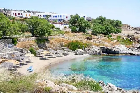 Rocky cove with turquoise water, sandy beach with sunbeds and white houses above
