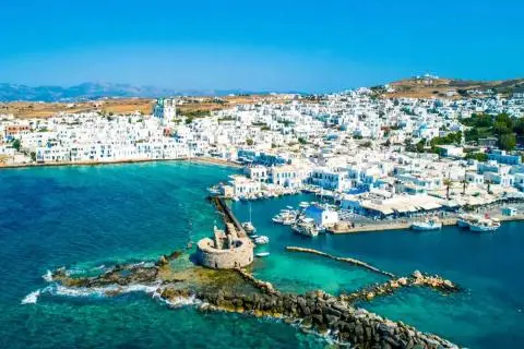Whitewashed coastal town with small marina, boats and stone pier with round fort