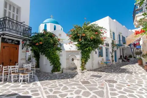Stone-paved alley with a blue-domed chapel, flowering vines and outdoor café chairs
