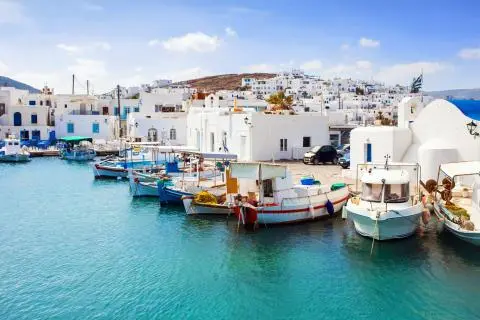 Colorful small fishing boats moored at a quay with white Cycladic houses above the turquoise water