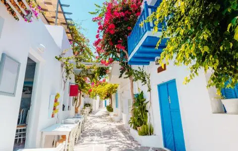 Narrow whitewashed lane with blue door and balcony, bougainvillea shading the stone pathway