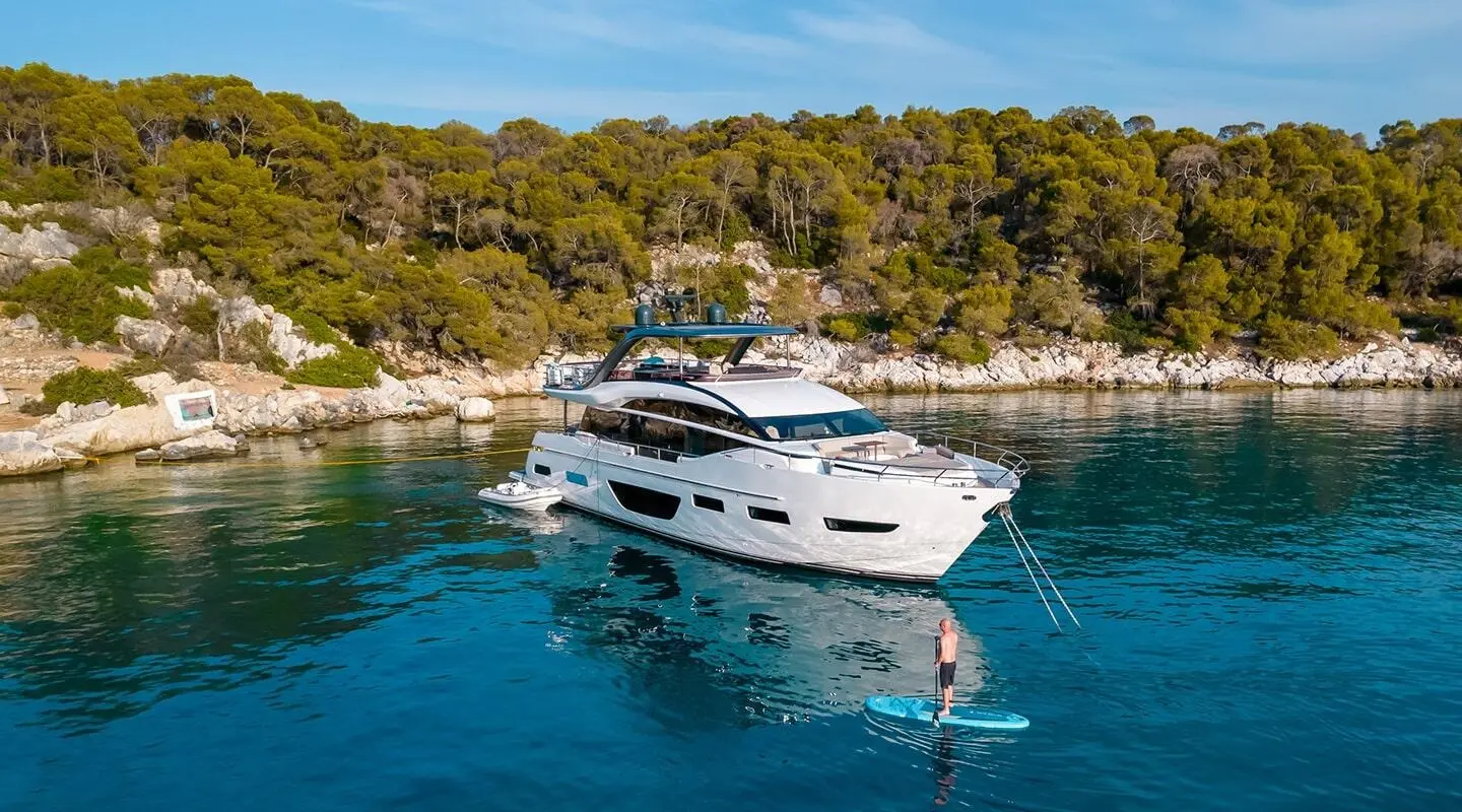 Yacht Vista anchored near rocky shoreline with clear blue water and trees