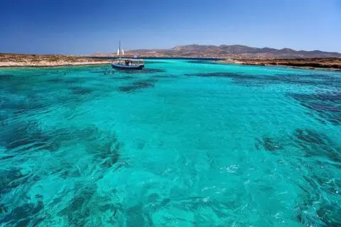White sailing boat and small vessel anchored near shore on vivid turquoise sea