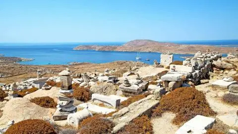 Blue bay with two sailboats and stacked stone cairns on rocky coastal hillside