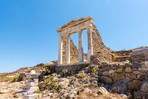 Ancient ruin with three marble columns on stone foundations under a clear blue sky