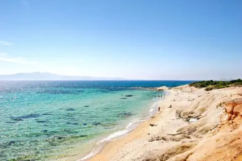 Turquoise sea, sandy shoreline and rocky cliffs on the right with a few people on the beach