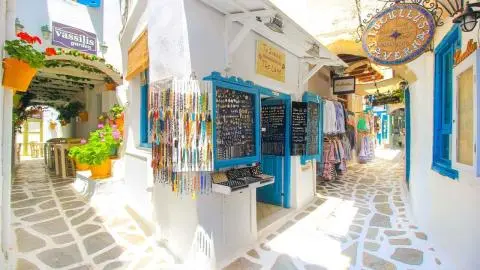 Narrow whitewashed Greek alley with blue-framed gift shop and hanging beaded necklaces