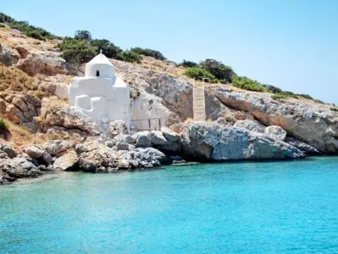 Small white chapel on rocky shore with steps and clear turquoise sea