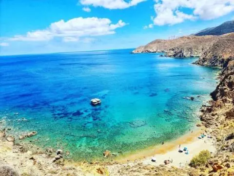 A turquoise-blue bay with a small anchored boat and a sandy cove seen from above
