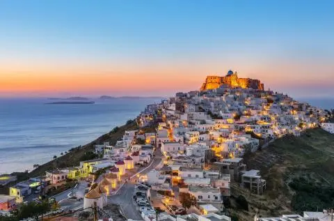 Sunset view of white hillside houses with lit fortress above and calm sea