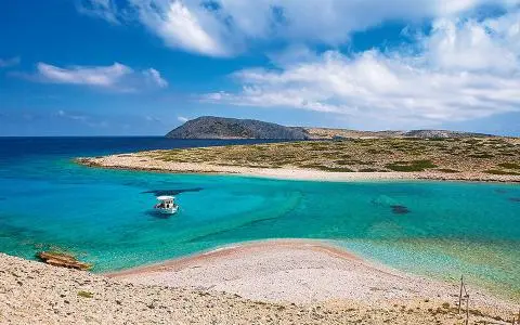 Small motorboat anchored in turquoise bay with rocky shoreline and distant island