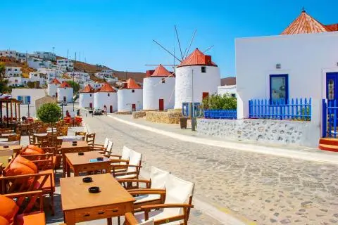 Cobblestone street with white windmills and outdoor cafe seating in a Greek island town