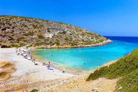 Pebble beach in a rocky cove with turquoise water and sunbathers on shore