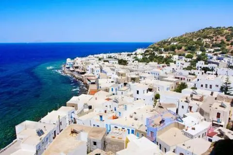 A coastal village of whitewashed houses on a hillside by deep blue sea, aerial view