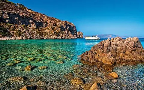 White motor yacht anchored off rocky coastline with clear turquoise shallow water