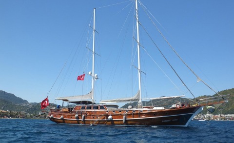 34m wooden sailing yacht Kaptan Mehmet Bugra anchored in blue waters with masts and Turkish flag visible
