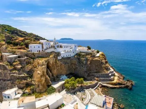Whitewashed buildings on a cliff above clear blue sea with terraces and winding coastal paths