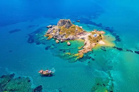 Small rocky islet with a chapel and a sailing boat in clear turquoise water