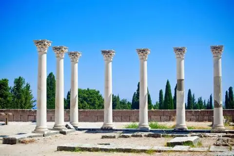 Row of eight marble columns and stone ruins against a clear blue sky