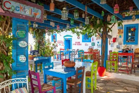 Open-air bar with colorful wooden tables and chairs, hanging lanterns and vine-covered pergola