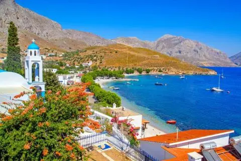 Blue-domed church bell tower, beachfront village, and boats on clear Mediterranean waters