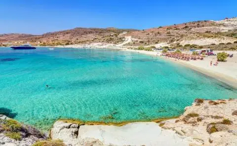 Turquoise bay with a luxury yacht anchored, sandy beach and arid hills in background