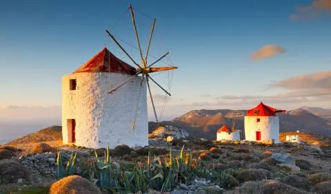 White stone windmills with red conical roofs on a hill at sunset