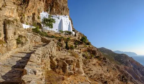 Whitewashed monastery on rocky cliff with stone steps and coastal sea and mountain view