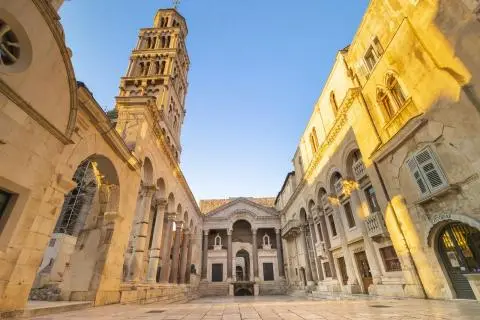 Stone Roman palace facade with colonnaded courtyard and bell tower at sunset