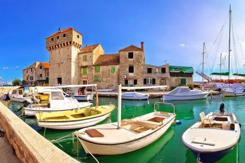 Historic stone tower beside a small marina with colorful small boats moored in clear green water