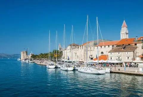 White sailing yachts moored along a waterfront with palm trees and historic stone buildings