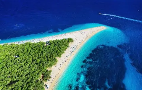 Aerial view of a tree-covered peninsula and narrow sandy spit surrounded by turquoise and deep blue sea